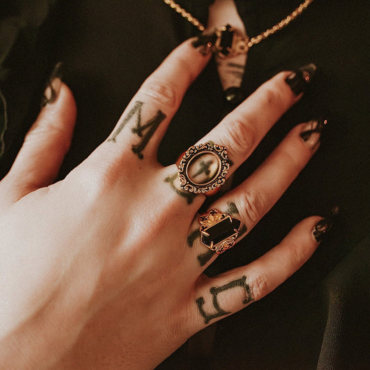 Hand with tattoos and ornate rings on a dark background