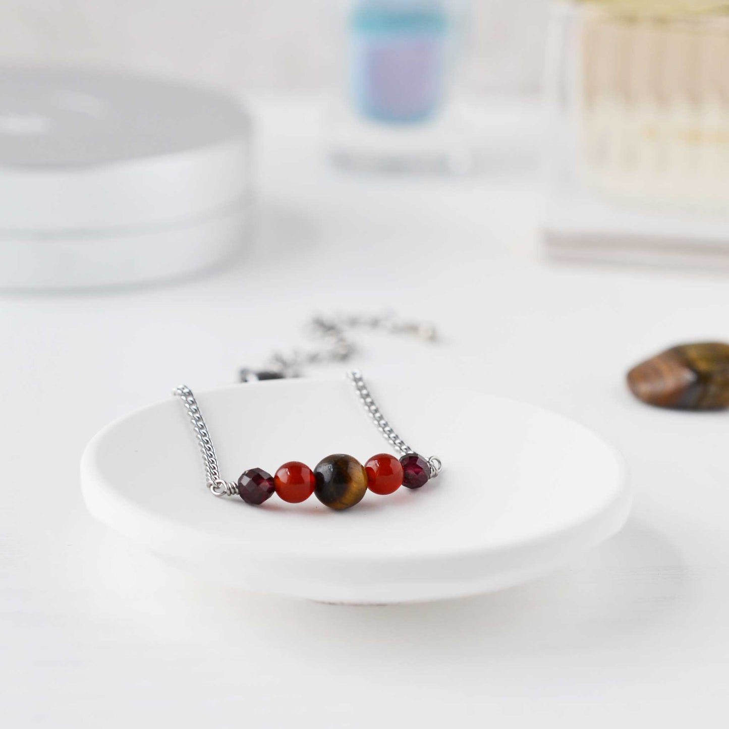 Dark dainty gemstone bracelet in trinket dish on dressing table