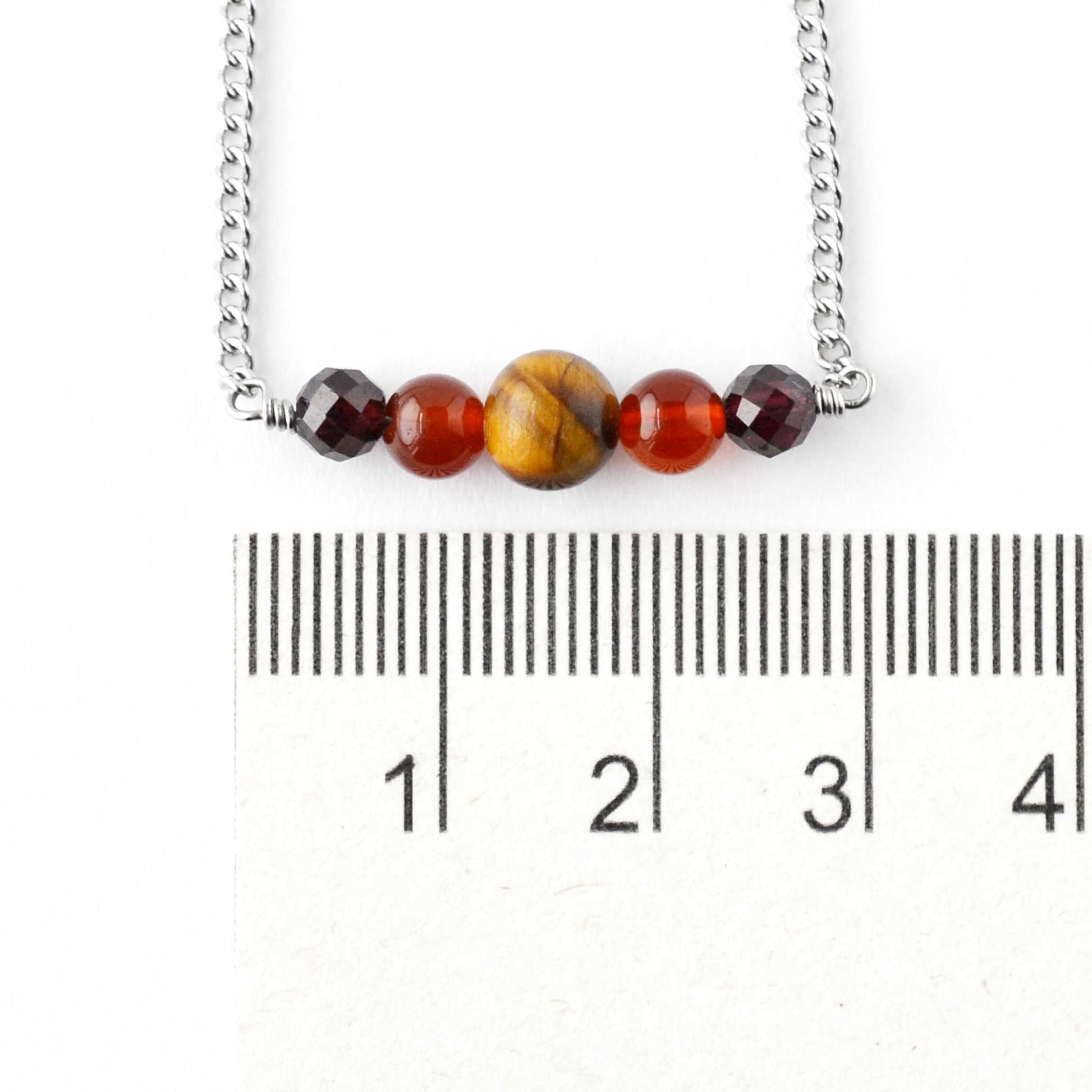 Dark gemstone bead necklace next to ruler