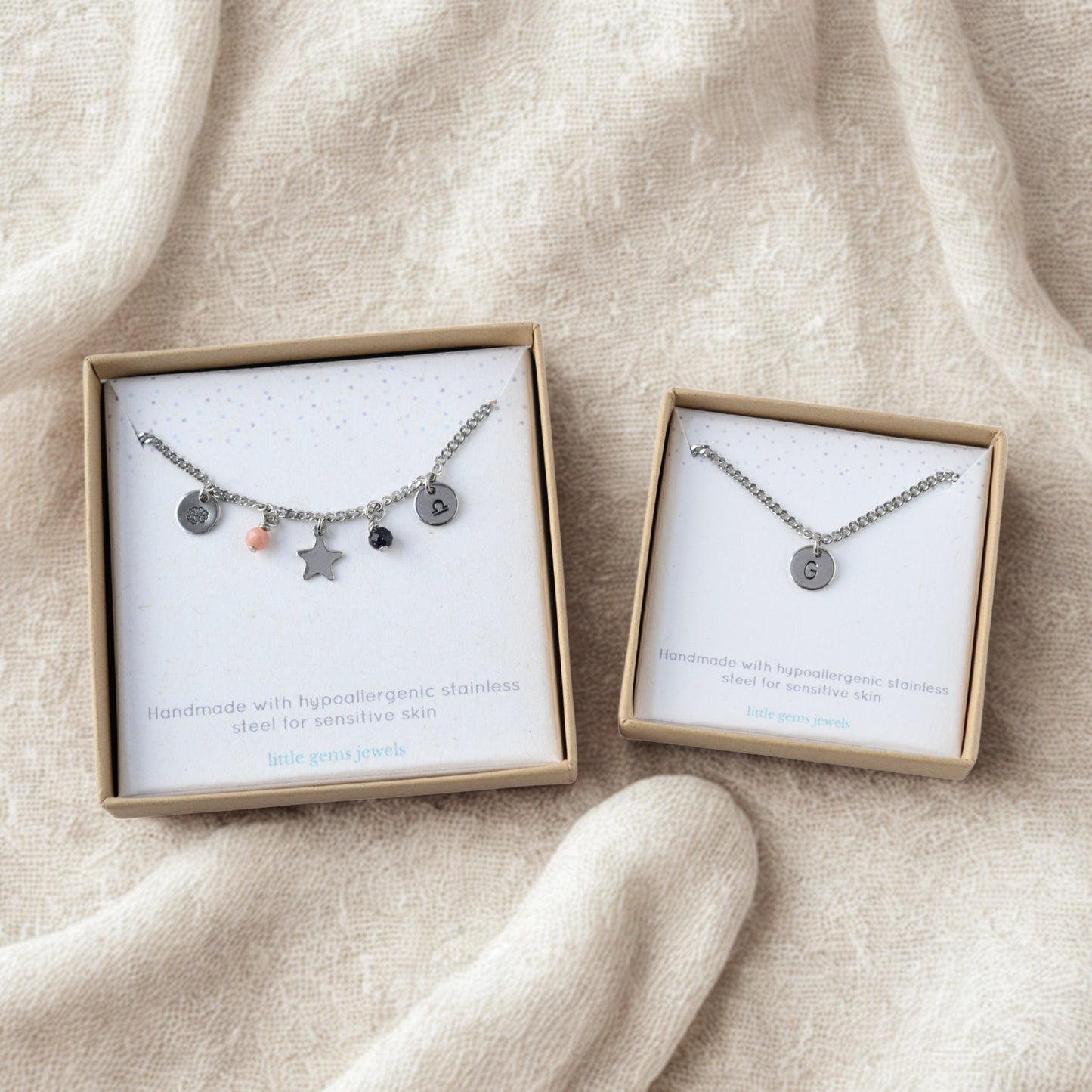 Single custom charm necklace and multi custom charm necklace in gift boxes laying on soft neutral fabric.