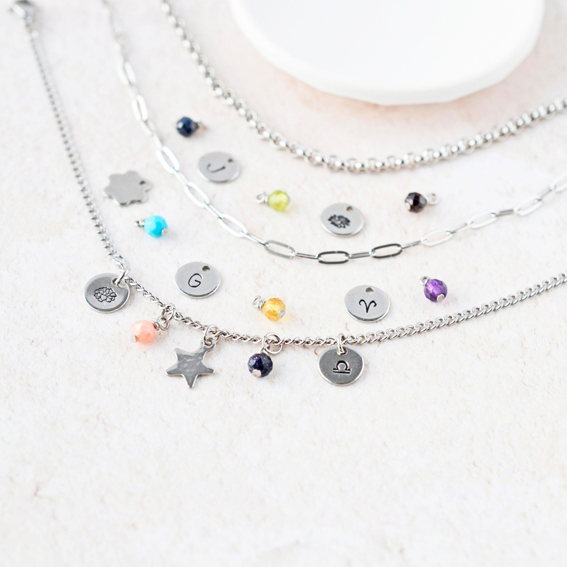 Close up of various tiny gemstone charms and hand stamped steel disc charms next to three different chain styles.