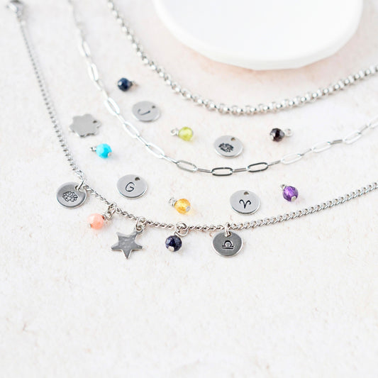 Close up of various tiny gemstone charms and hand stamped steel disc charms next to three different chain styles.