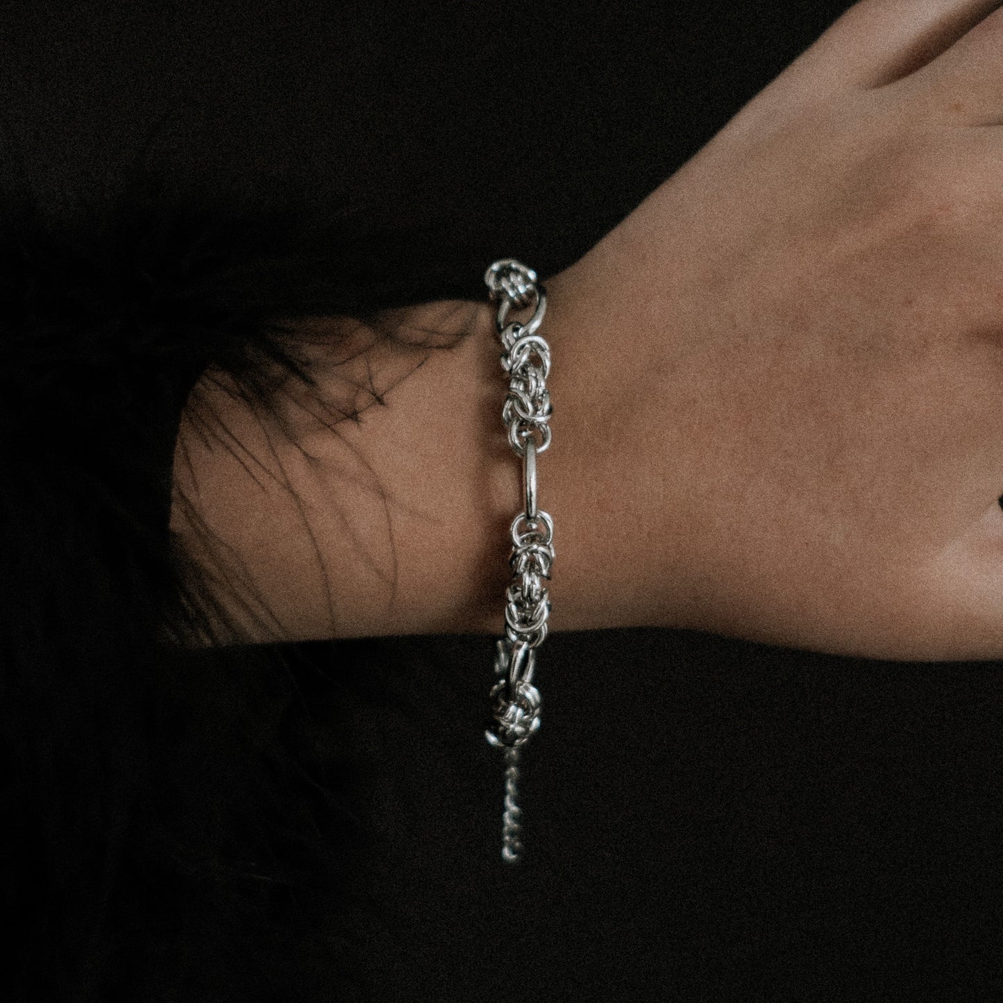 Steel chain bracelet on a wrist against a dark background