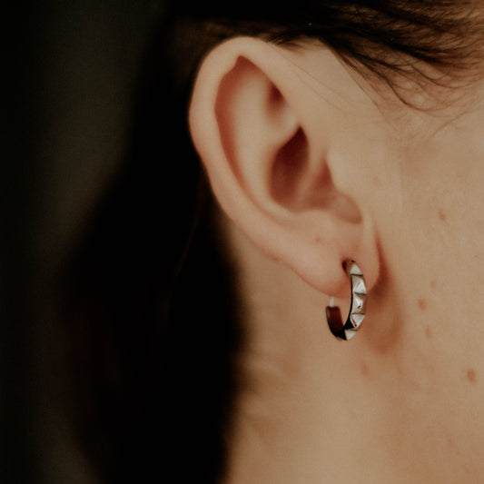 Close-up of an ear wearing a small hoop earring with a dark background