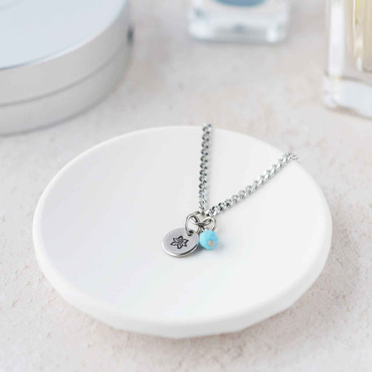 Tiny Poinsettia & Turquoise gemstone necklace laying in white trinket dish