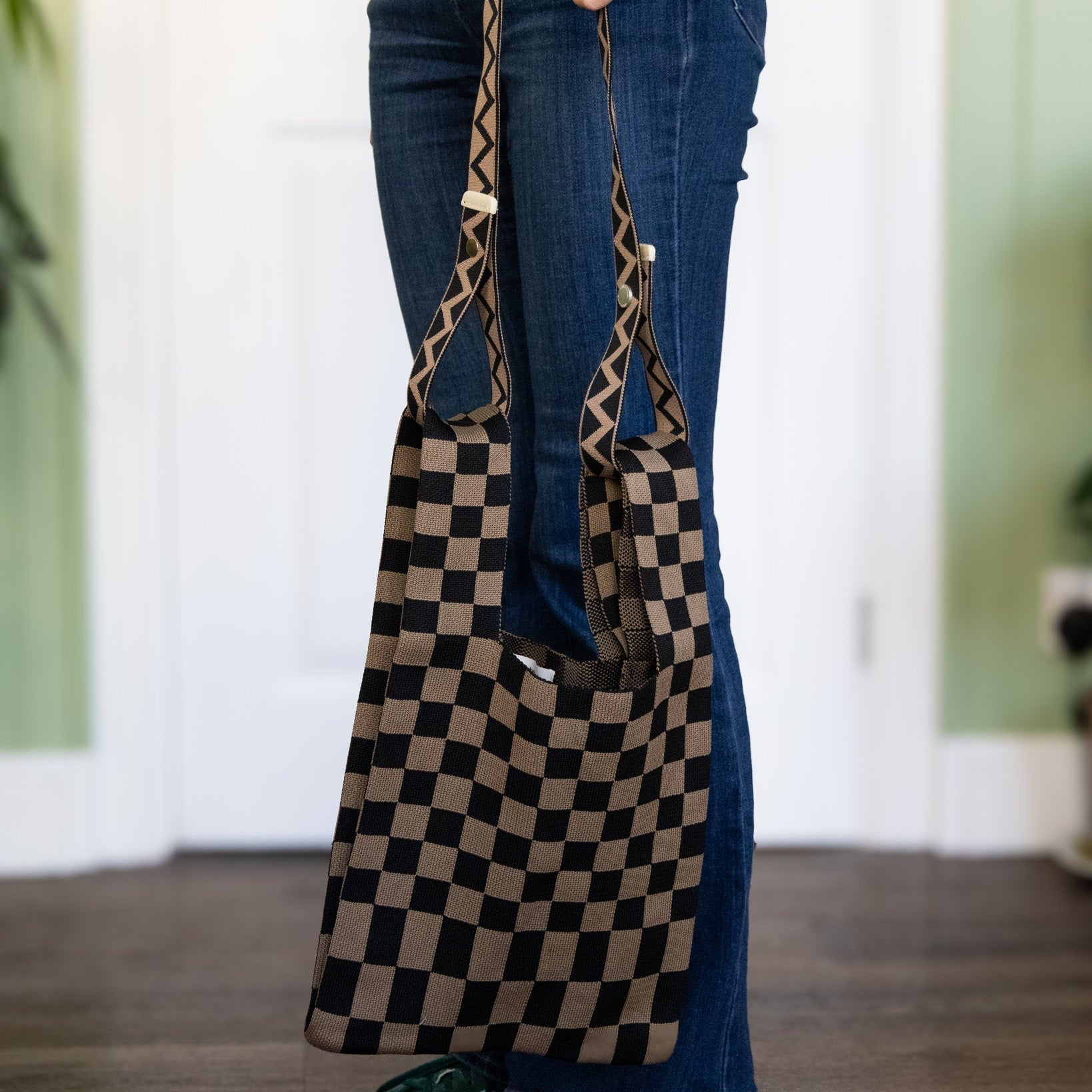 Person holding a checkered bag with a leopard print strap indoors.