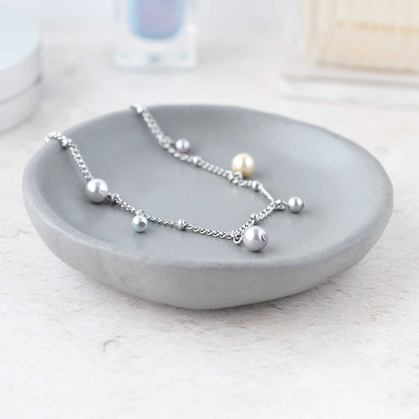 Dainty faux pearl charms bracelet in grey trinket dish on dressing table.