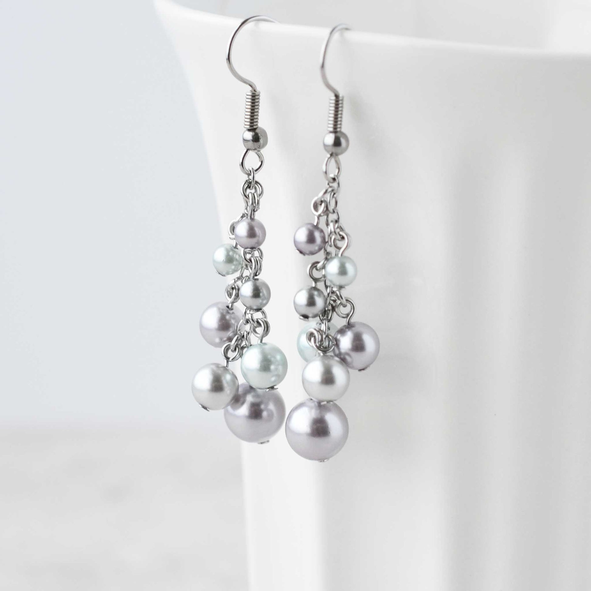 Faux pearl cluster drop earrings hanging on edge of white cup.
