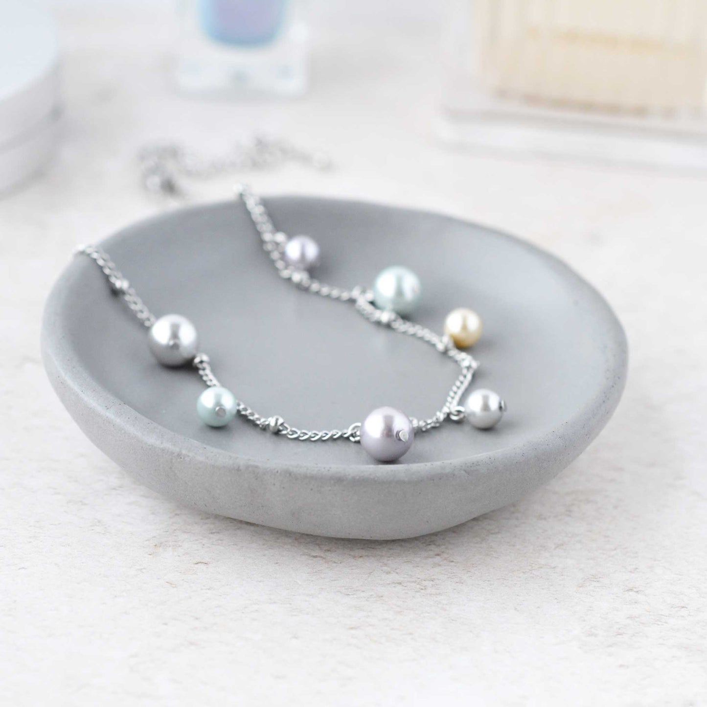 Dainty faux pearl charms necklace lying in grey trinket dish on dressing table.