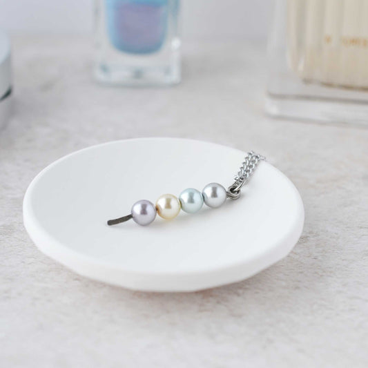 Faux pearl stacked pendant necklace lying in trinket dish on dressing table.