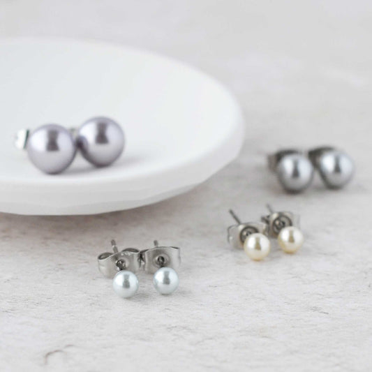 Four pairs of faux pearl stud earrings next to white trinket dish.