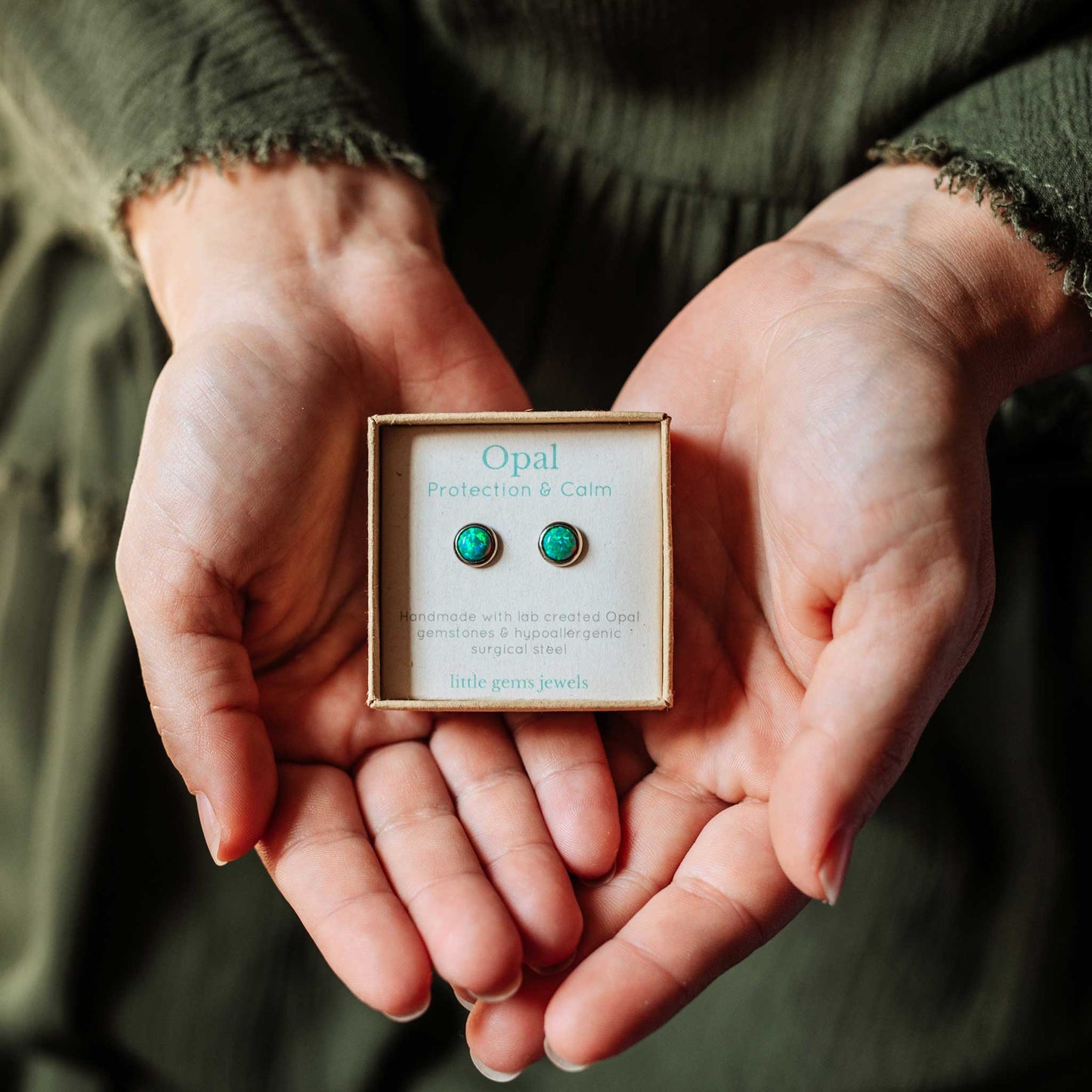 Hands holding a box of Opal earrings with a green gemstone.