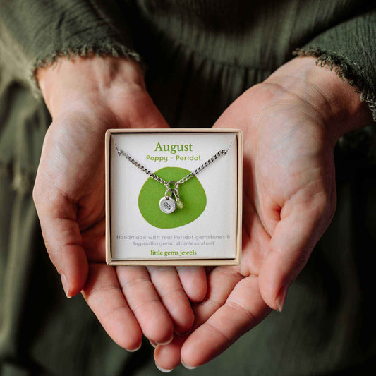 Woman's hands holding a small square eco-friendly gift box containing a dainty August birthflower with Peridot birthstone necklace