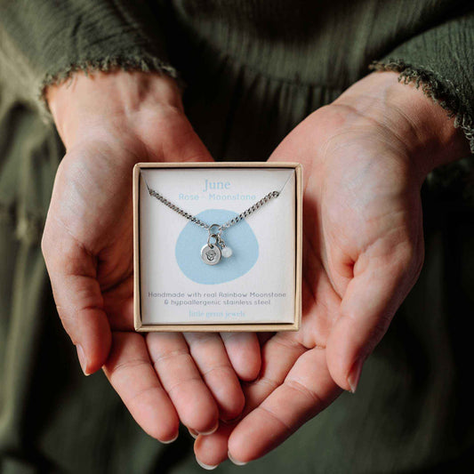 Woman's hands holding a small square eco-friendly gift box containing a dainty June birthflower with Moonstone birthstone necklace