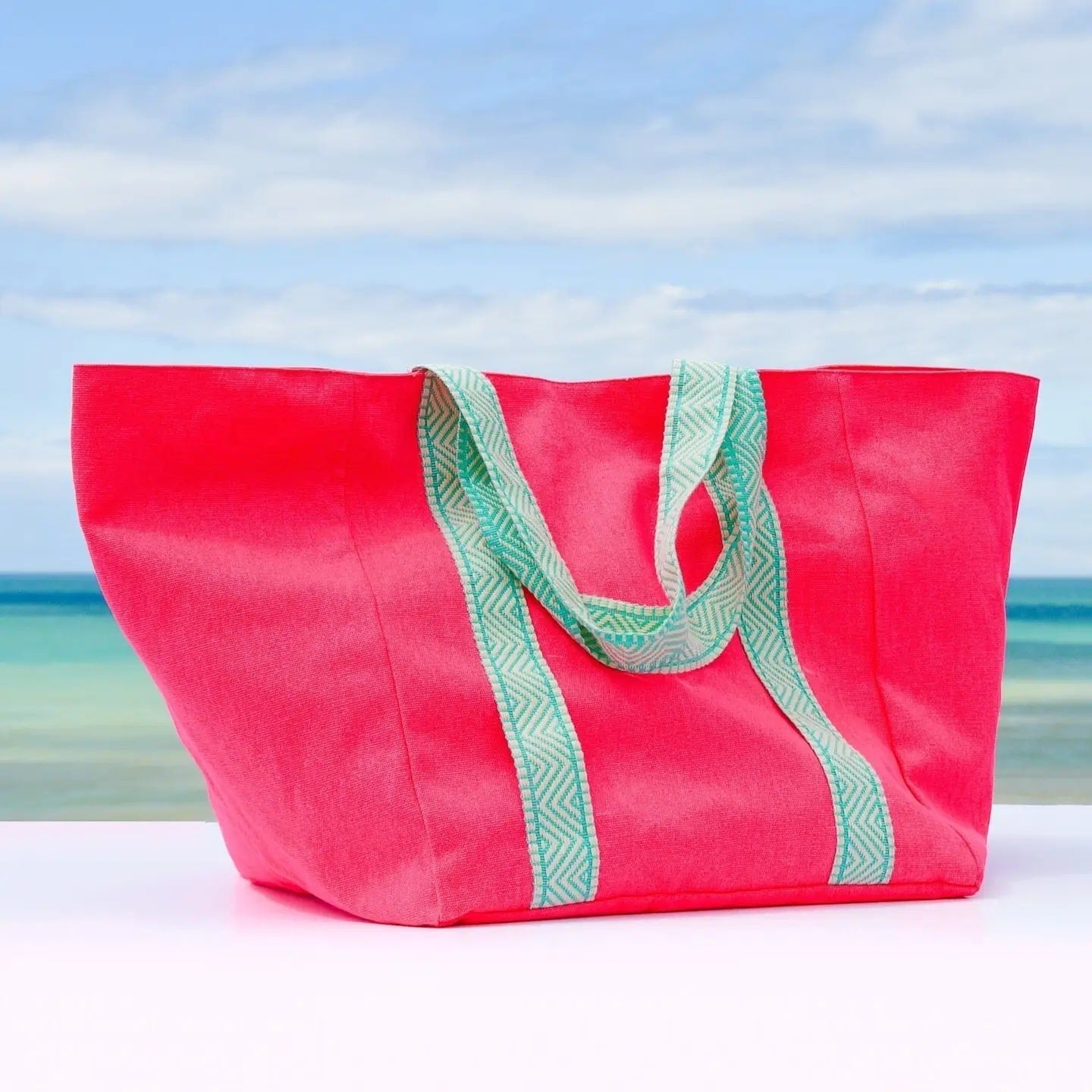 Pink tote bag with green handles on a white surface with a beach background
