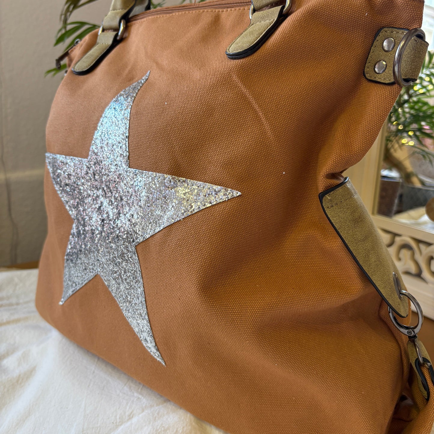 Brown tote bag with a large silver star on a light-colored surface.