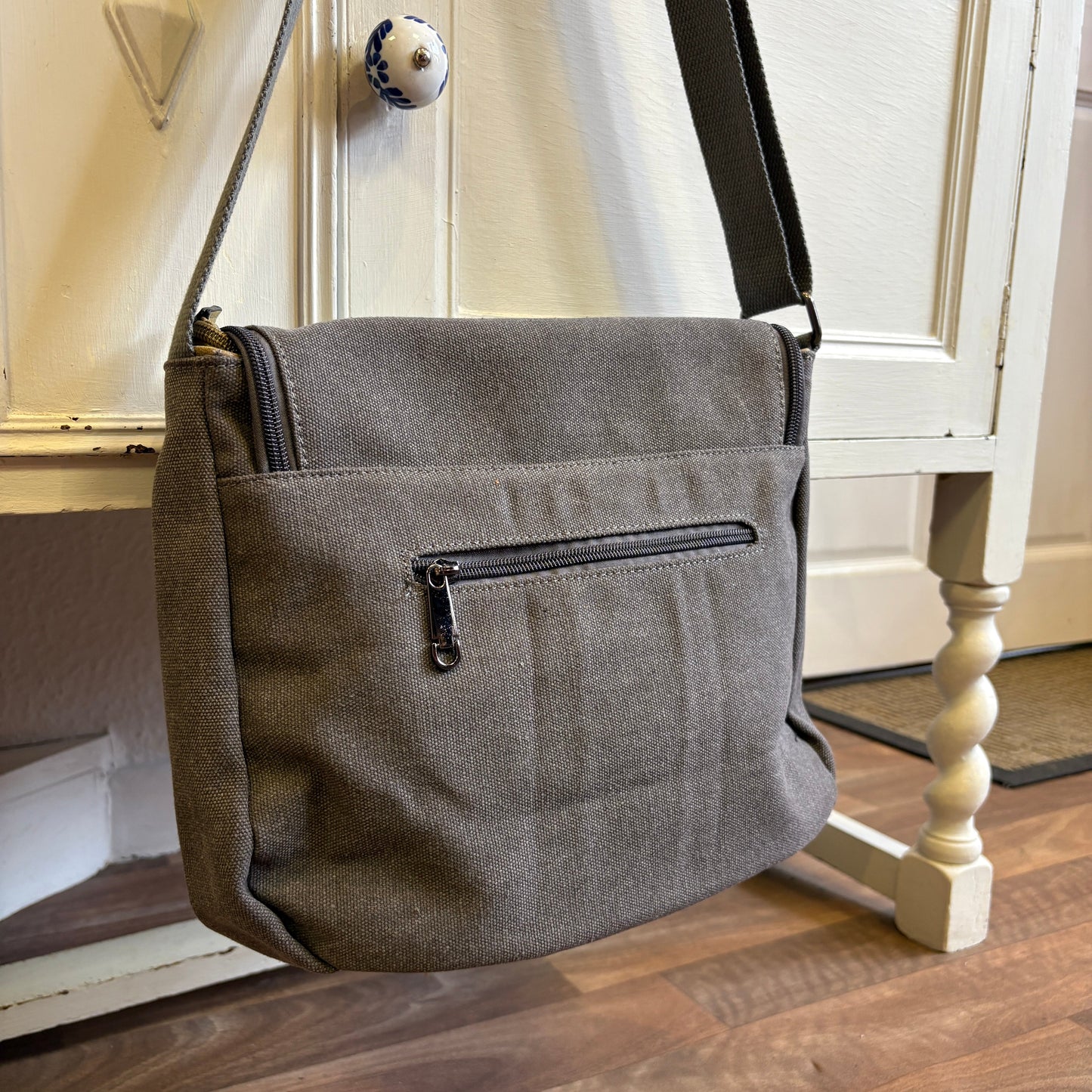 Gray shoulder bag on a wooden floor with a white cabinet in the background