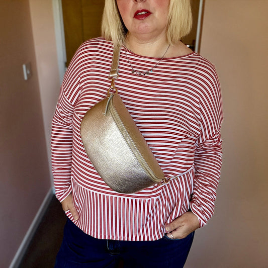Person wearing a red and white striped shirt holding a gold handbag indoors.