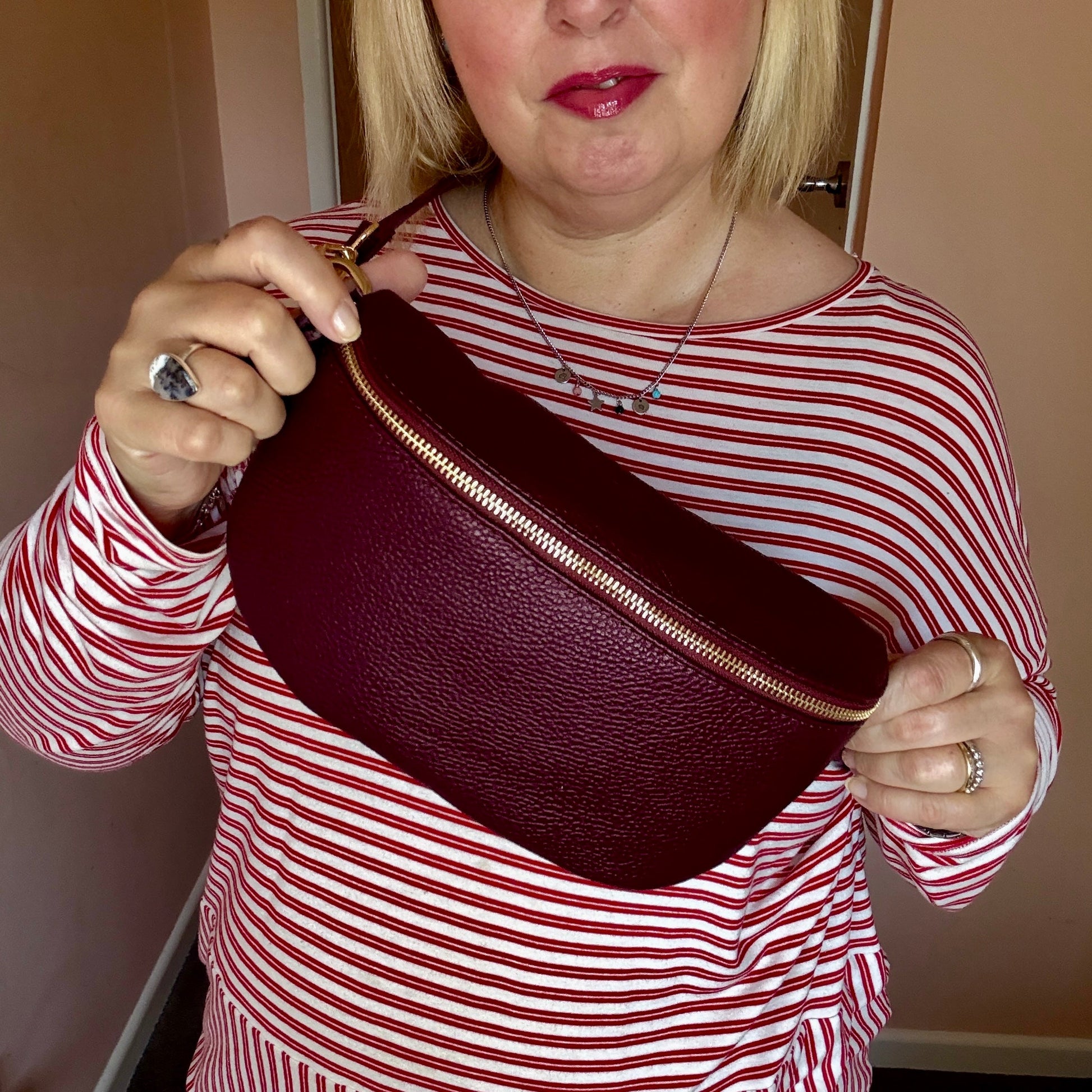 Woman holding a burgundy leather bag with gold zipper against a neutral background