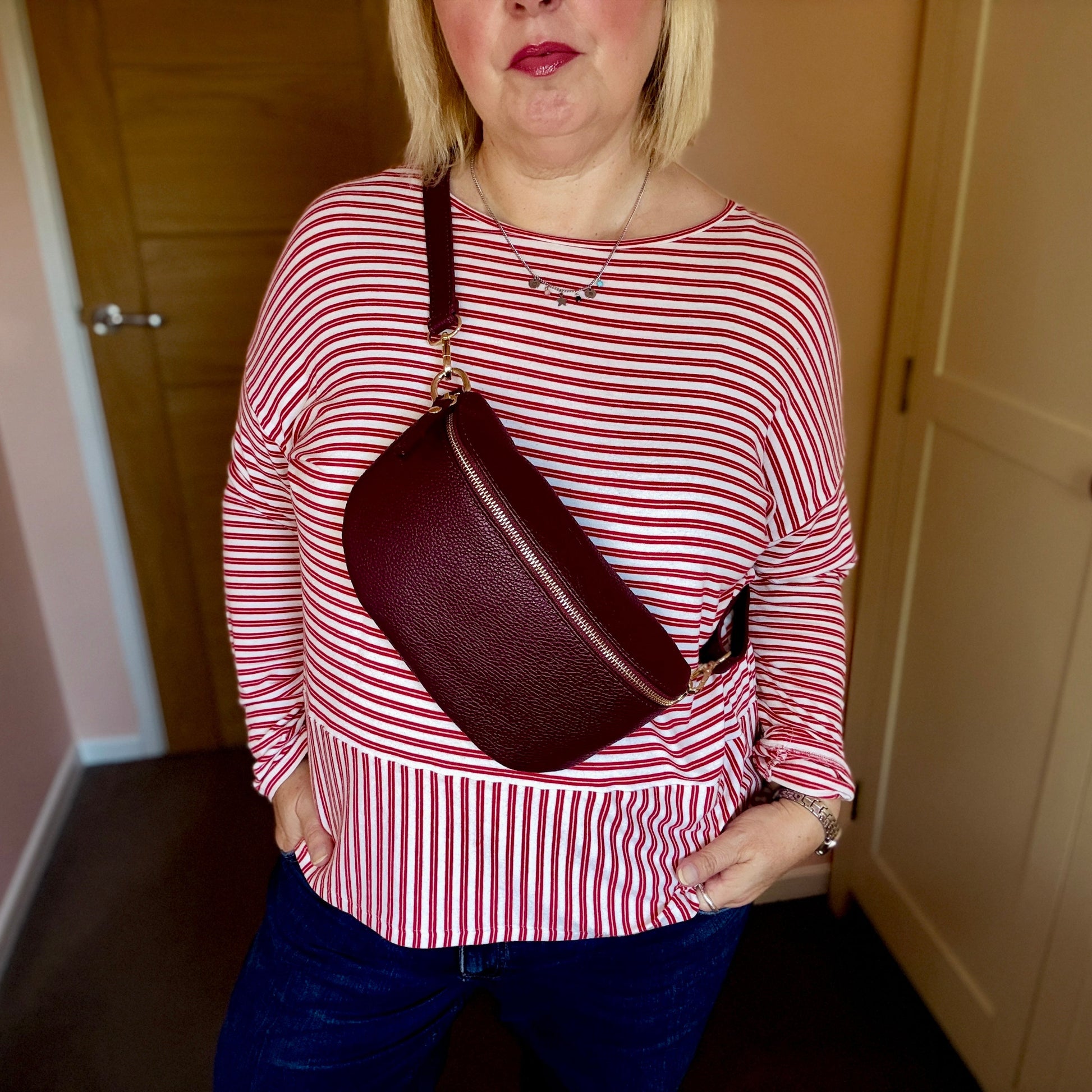 Person wearing a red and white striped shirt holding a maroon handbag indoors.