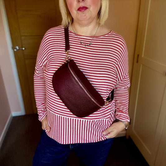Person wearing a red and white striped shirt holding a maroon handbag indoors.