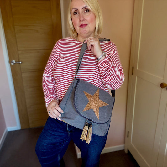 Woman holding a gray crossbody bag with a star design in a room.