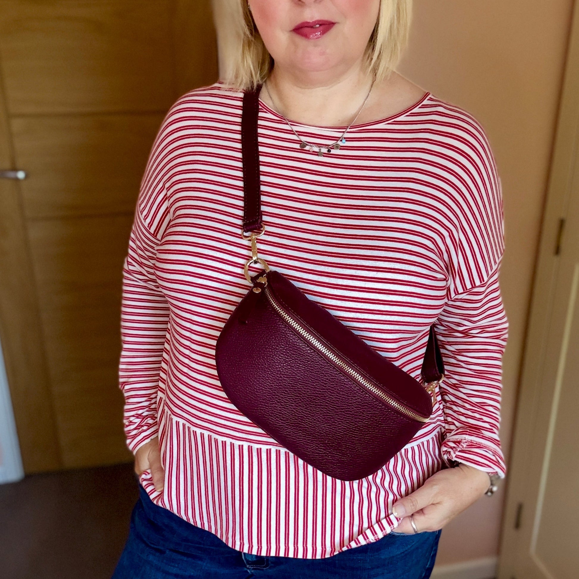 Woman wearing a red and white striped shirt and blue jeans, holding a maroon handbag indoors.