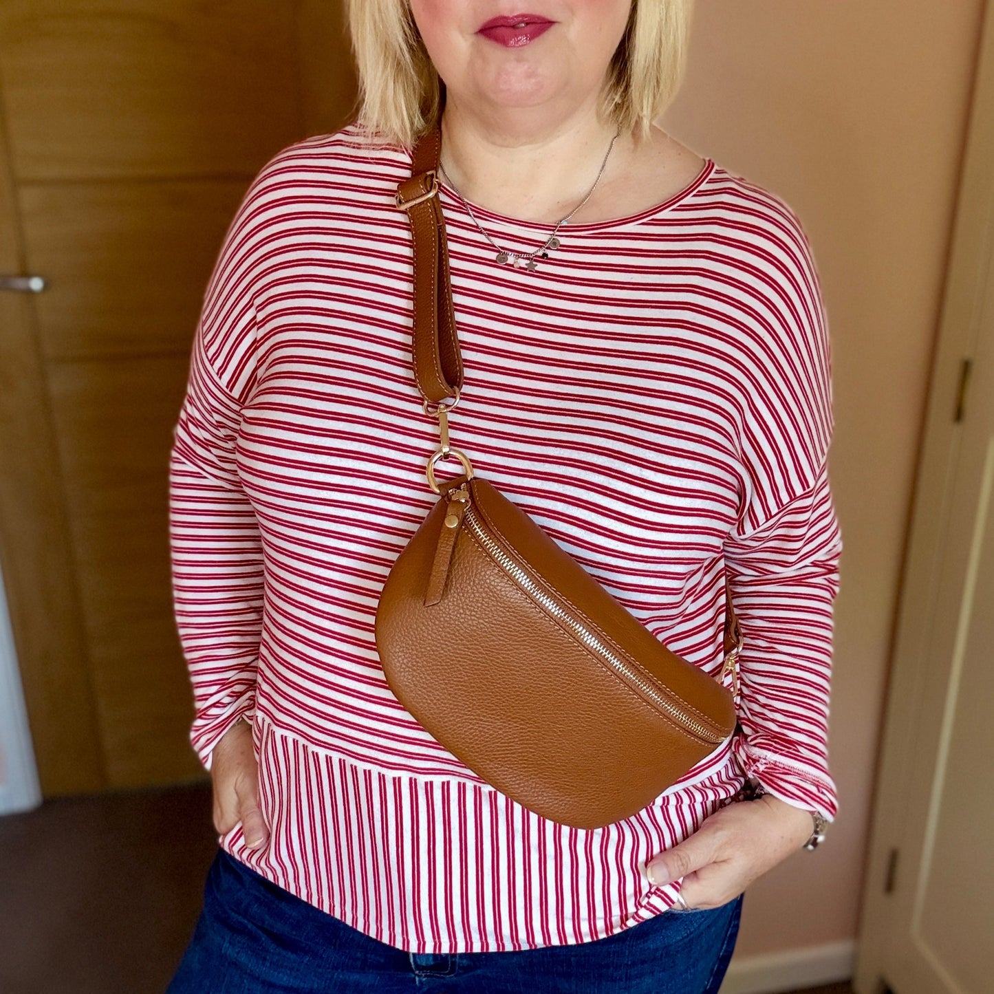 Woman wearing a red and white striped shirt and blue jeans, holding a brown handbag indoors.