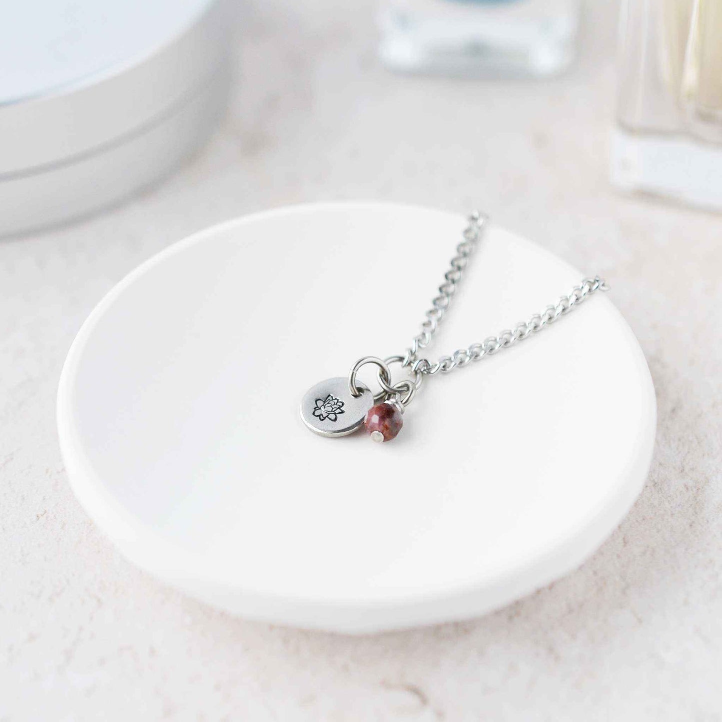 Tiny Lotus flower & Ruby gemstone necklace laying in white trinket dish