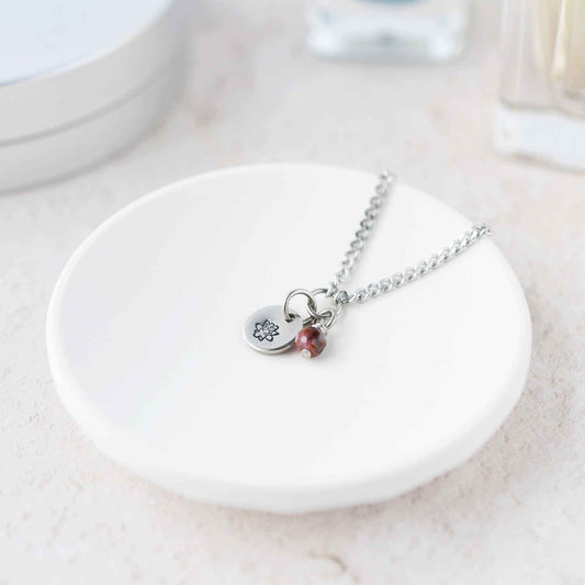 Tiny Lotus flower & Ruby gemstone necklace laying in white trinket dish