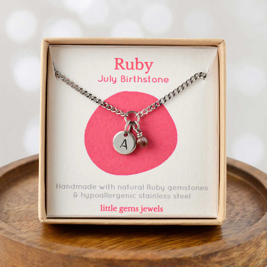 Ruby July Birthstone necklace with hand stamped initial inside an eco-friendly gift box sitting on wooden coaster
