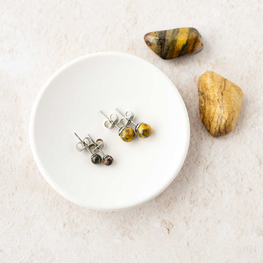 Two pairs of Leopardskin Jasper stud earrings laying in a white trinket dish with jasper stones in background.