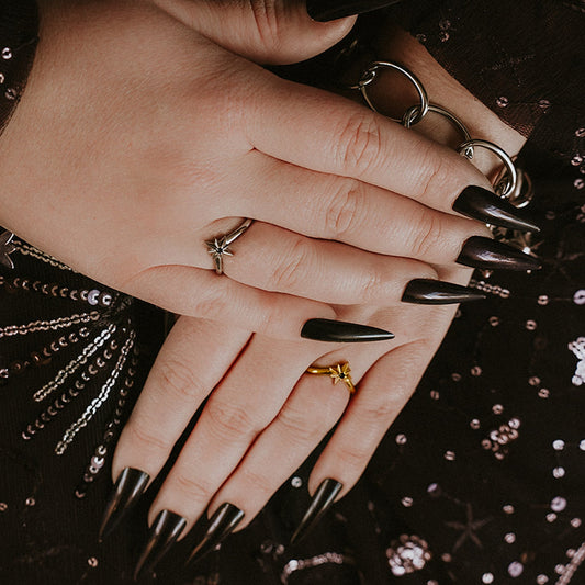 Close-up of a hand with black nail polish and multiple rings on a dark background