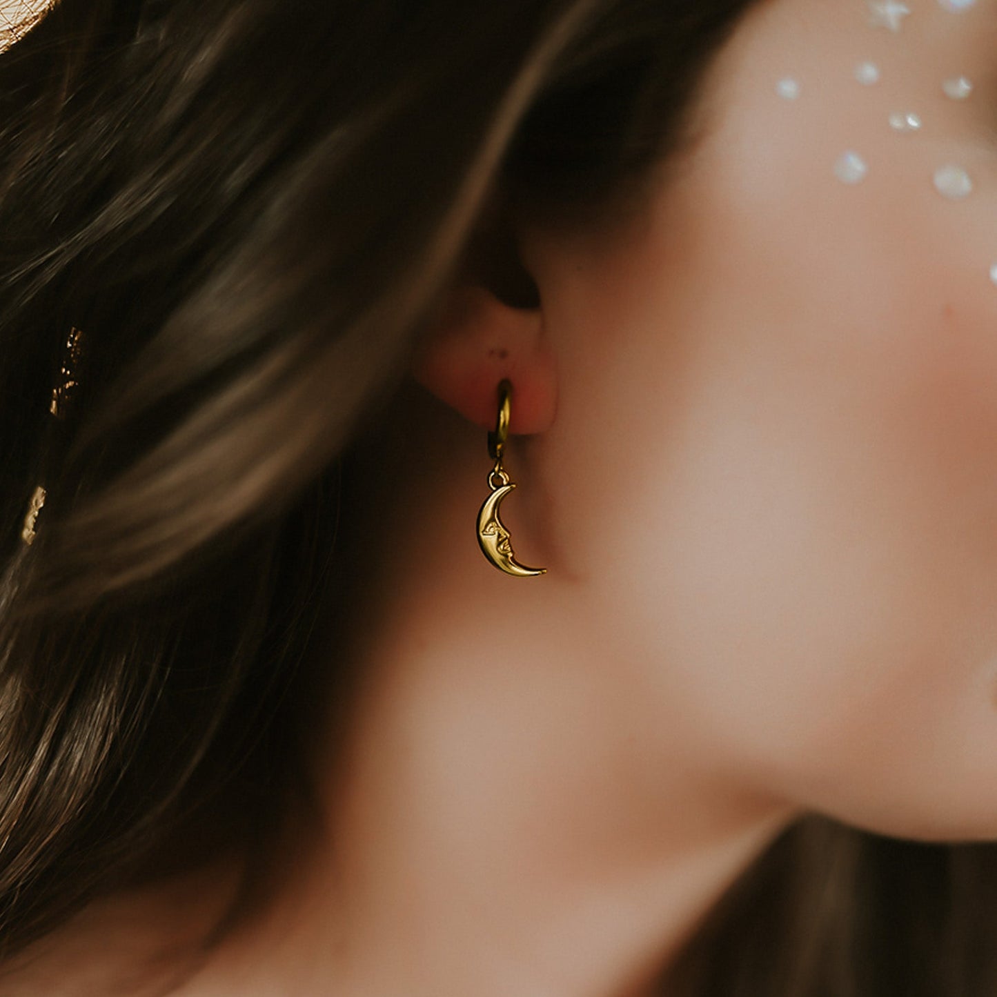 Close-up of an ear wearing a gold moon-shaped earring with blurred hair and skin in the background.