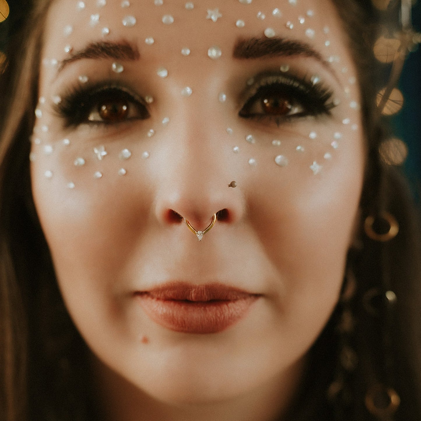 Close-up of a person with decorative face makeup and a gold nose ring.