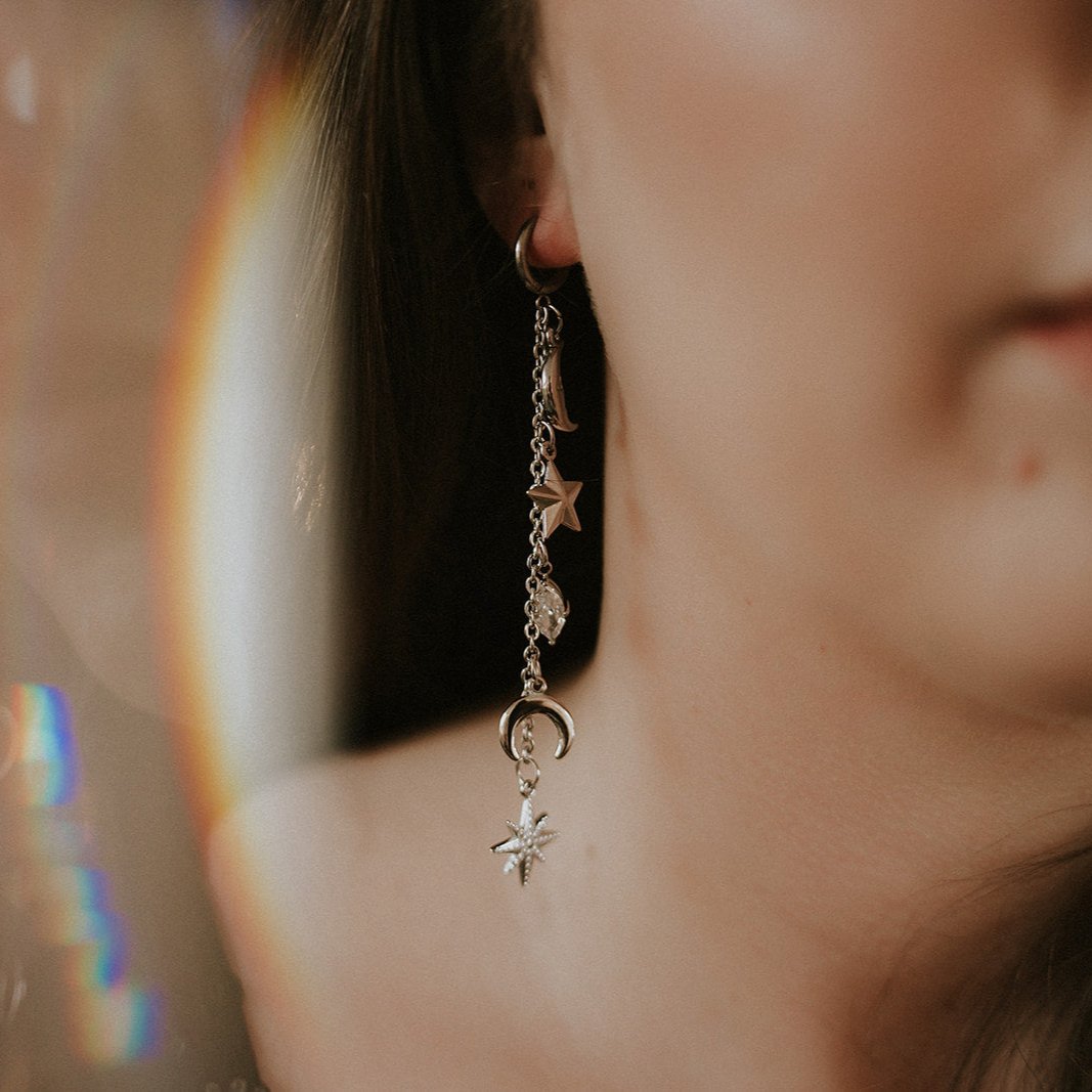 Close-up of a person wearing a drop earring with star and moon charms.