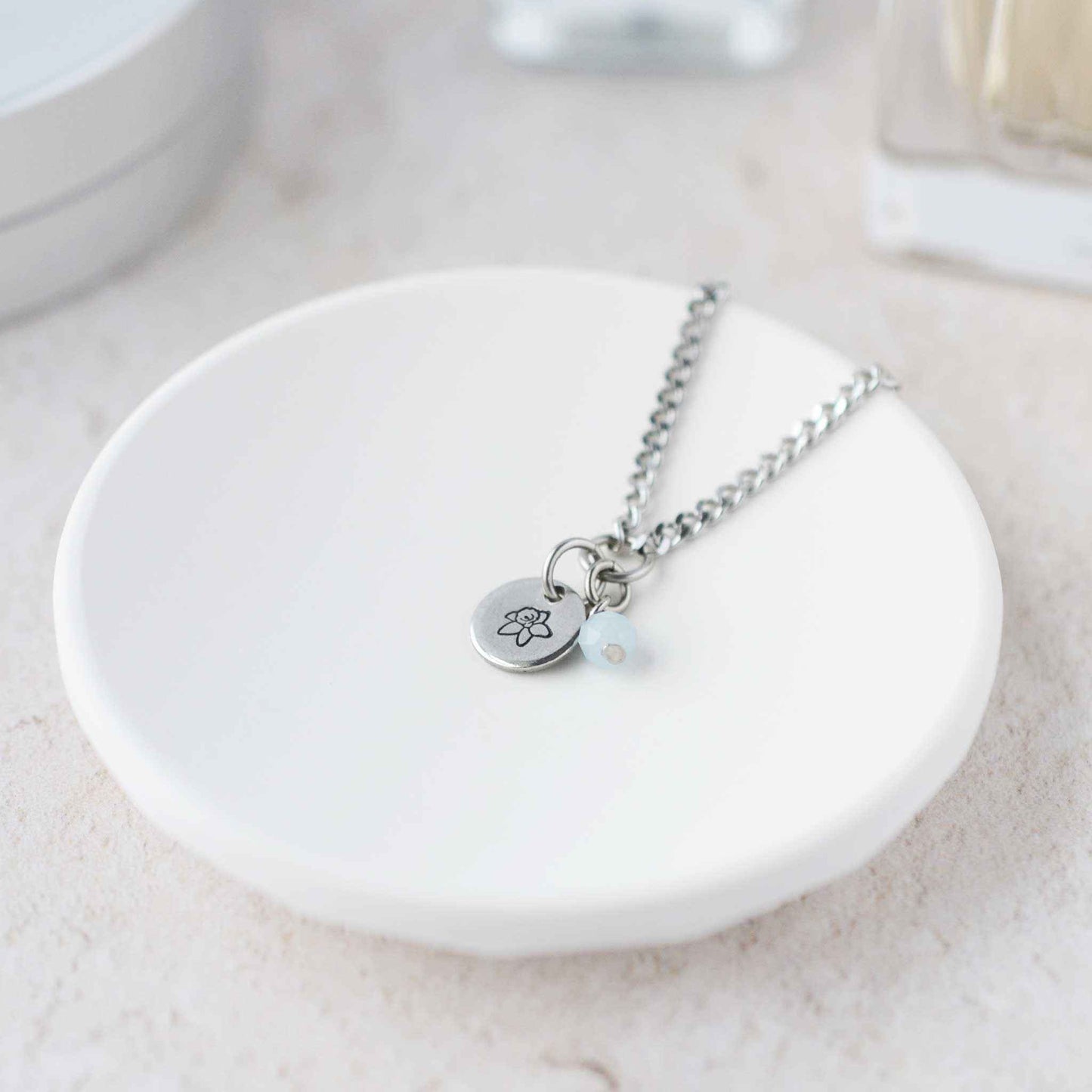 Tiny Daffodil & Aquamarine gemstone necklace laying in white trinket dish