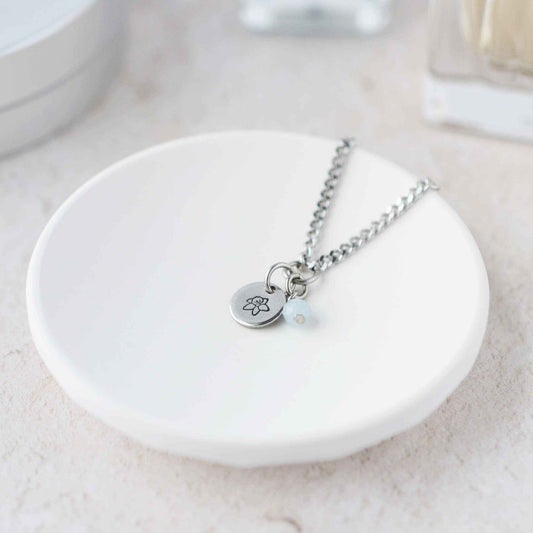 Tiny Daffodil & Aquamarine gemstone necklace laying in white trinket dish