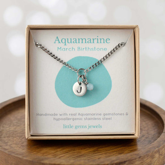 Aquamarine March Birthstone necklace with hand stamped initial inside an eco-friendly gift box sitting on wooden coaster