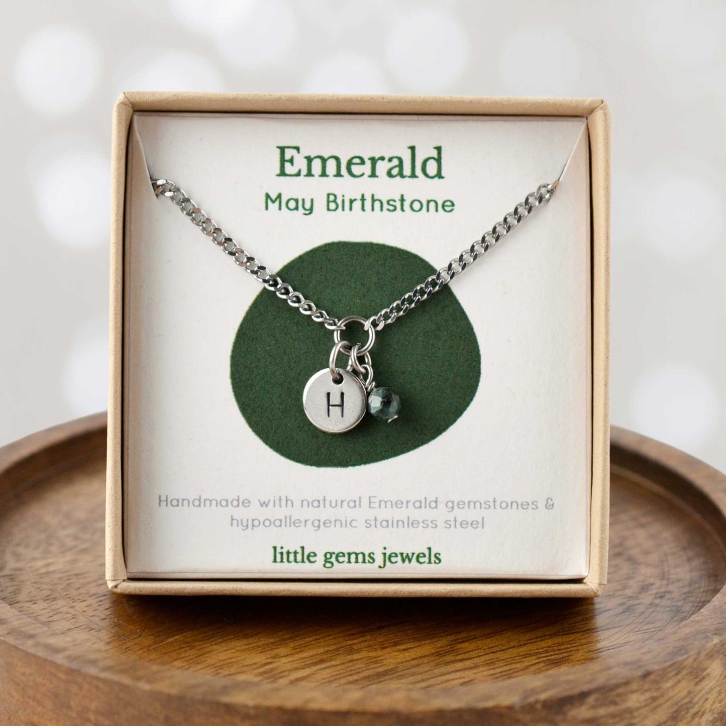 Emerald May Birthstone necklace with hand stamped initial inside an eco-friendly gift box sitting on wooden coaster