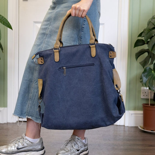 Person holding a blue handbag with beige handles and straps in an indoor setting.