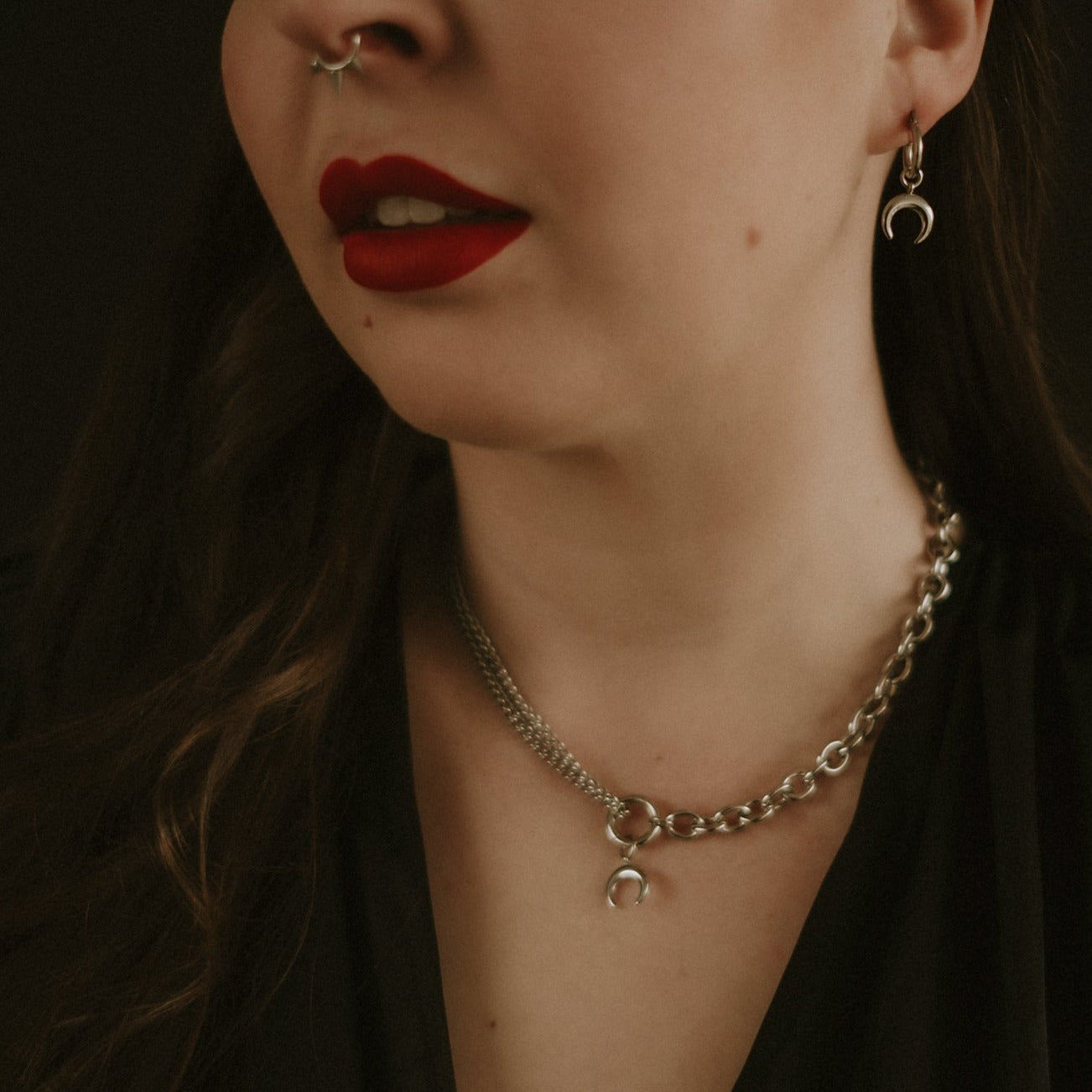 Close-up of a person wearing a chain necklace with a small pendant, against a dark background.