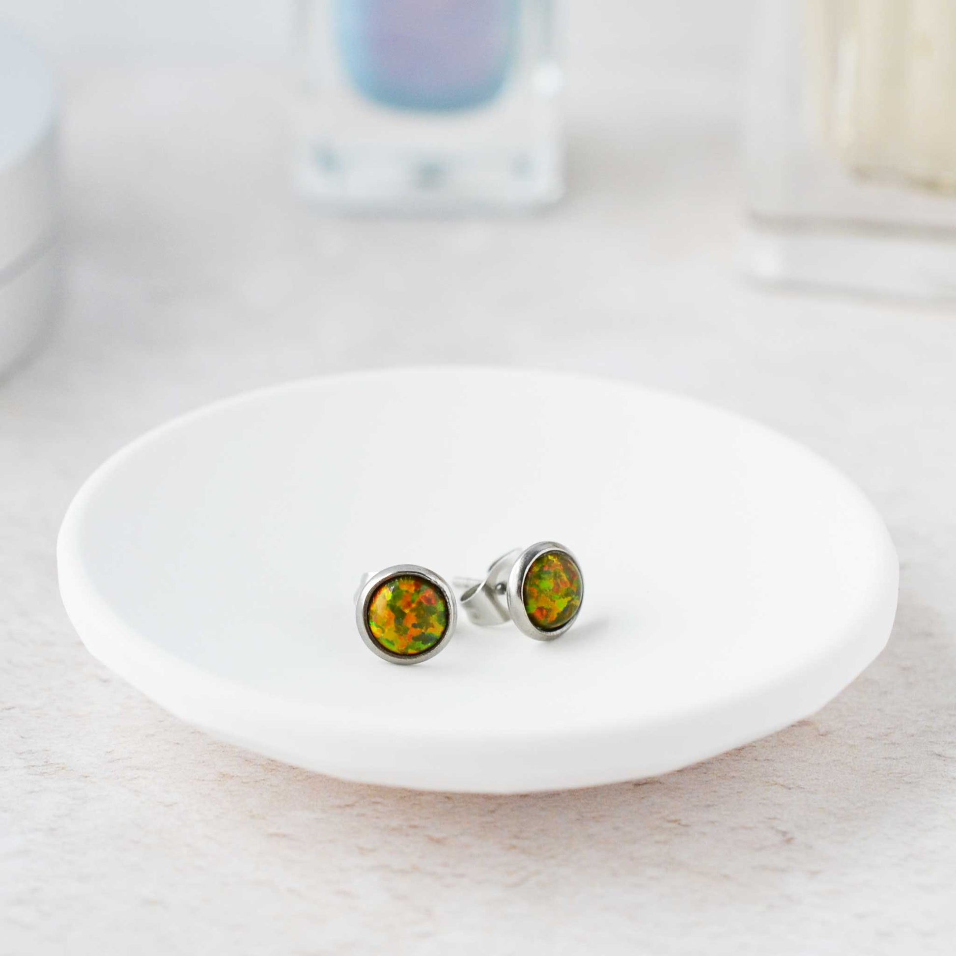 Opal stud earrings on a white dish with a blurred background