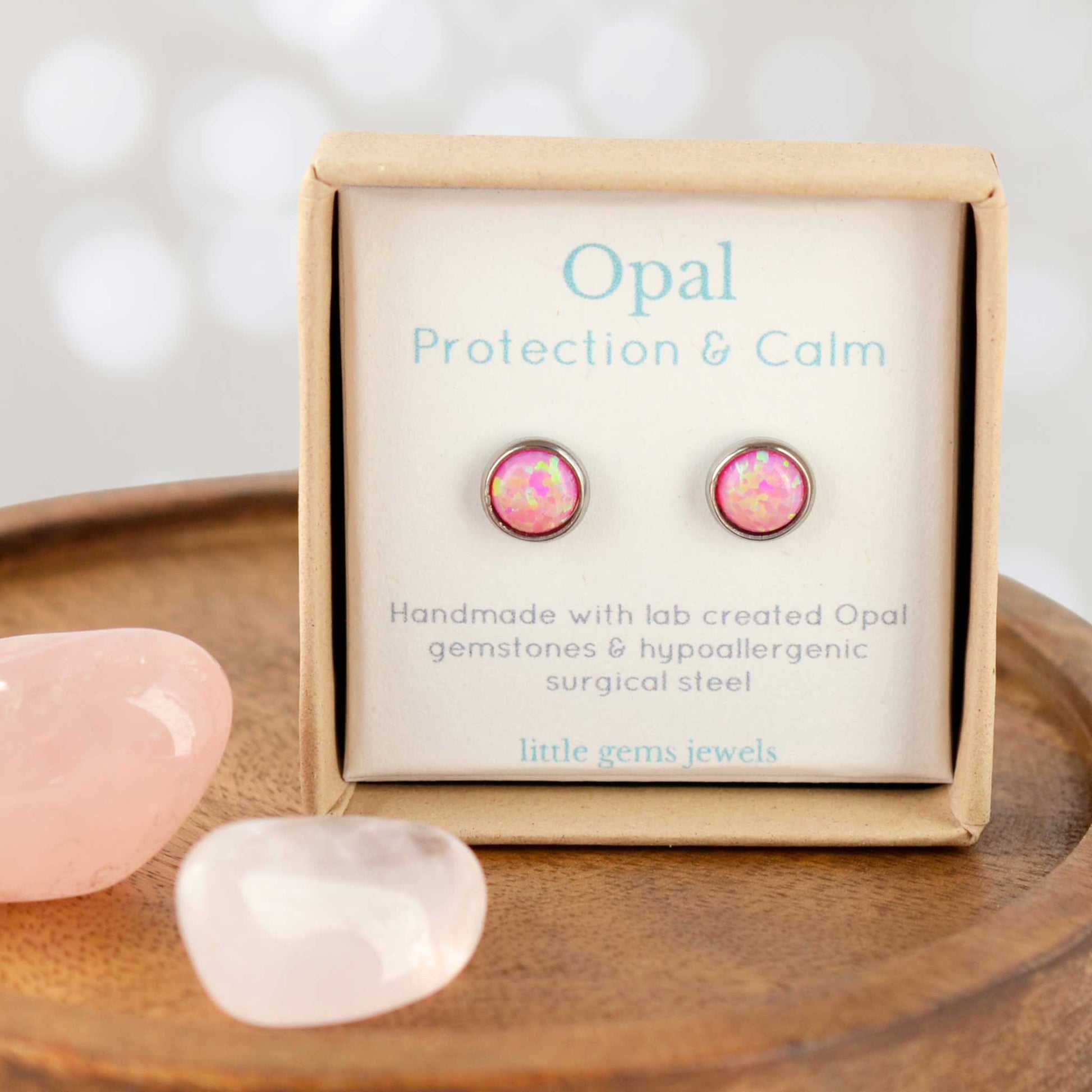 Pink Opal earrings in a box with stones on a wooden surface