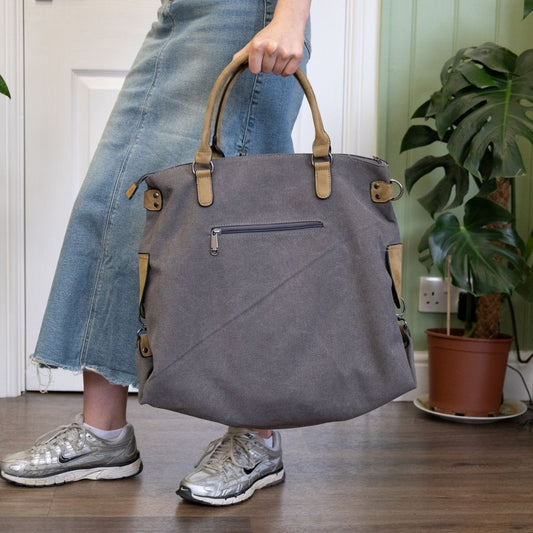 Person holding a gray handbag indoors with a plant in the background