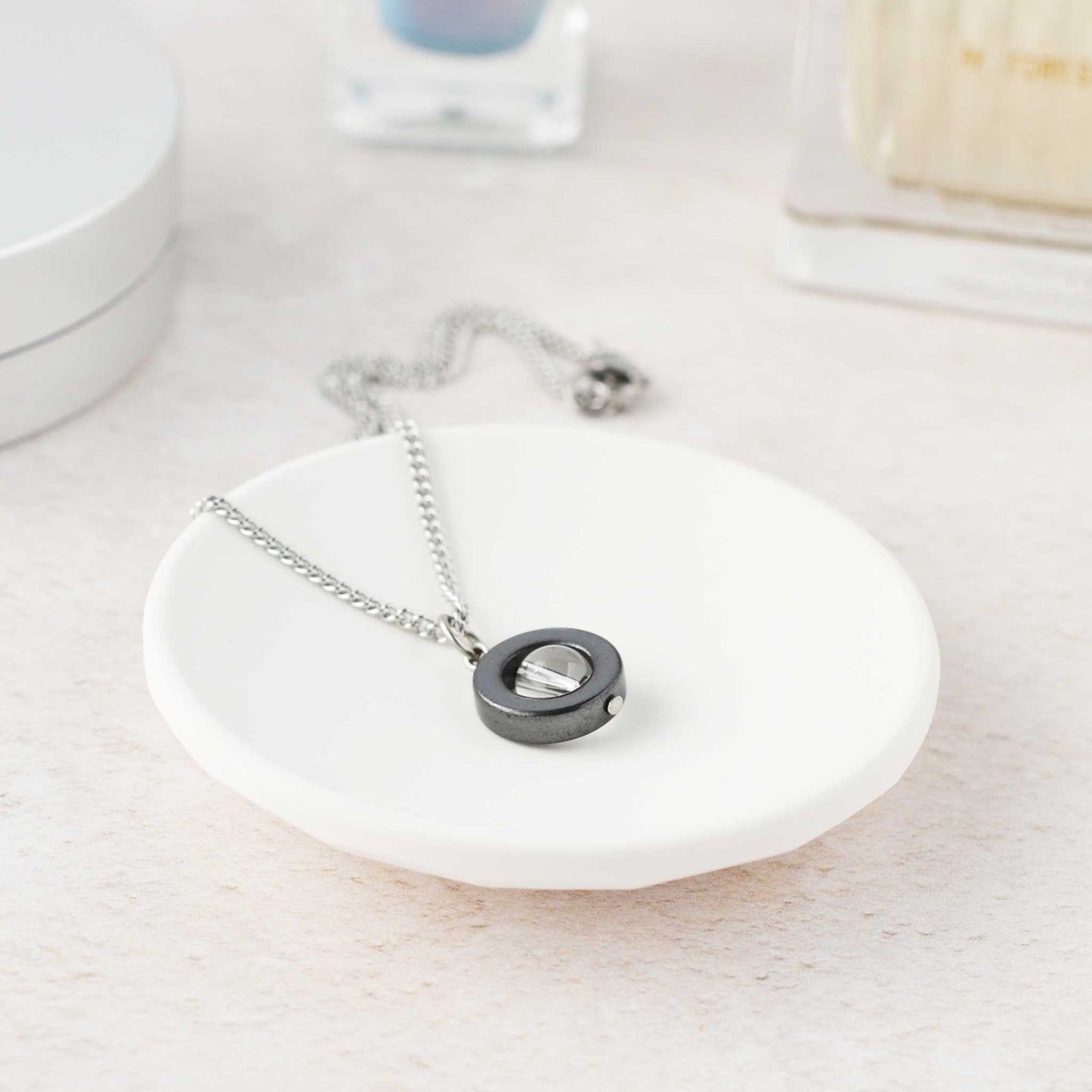 Dainty clear crystal gemstone spinner necklace lying in trinket dish on dressing table.