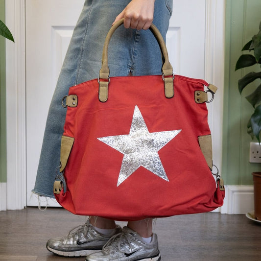 Red bag with a silver star held by a person wearing jeans and silver shoes.