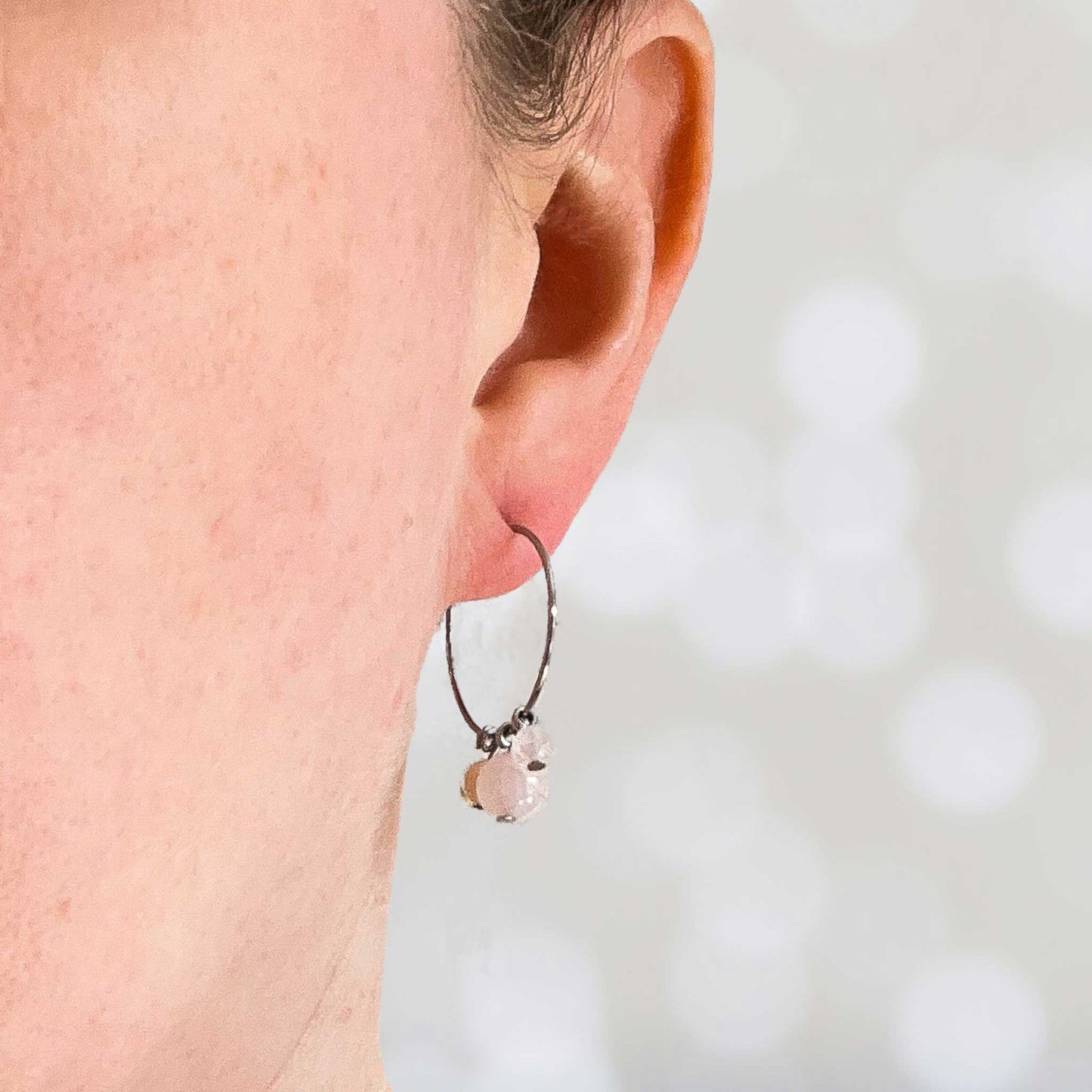 Woman wearing pale pink gemstone hoop earring in earlobe