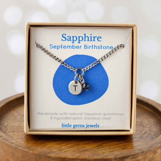 Sapphire September Birthstone necklace with hand stamped initial inside an eco-friendly gift box sitting on wooden coaster