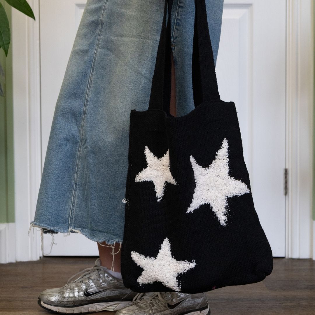 Person holding a black tote bag with white stars, wearing blue jeans and silver shoes.